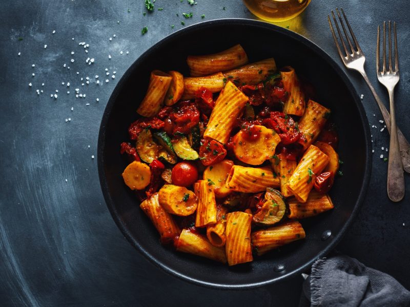 Tasty appetizing vegetarian pasta with vegetables and tomato sauce served on pan. Closeup.